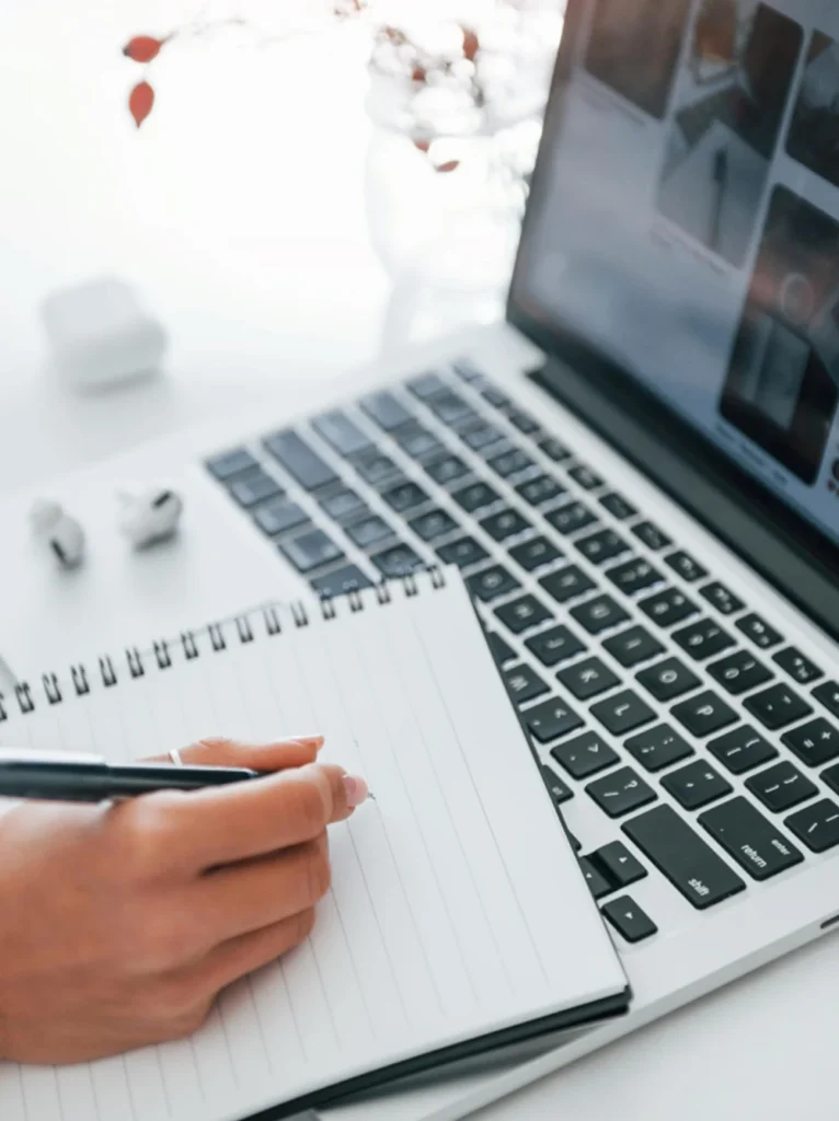 Mano escribiendo en una libreta junto al portátil, representando la toma de apuntes y reflexiones sobre cursos online