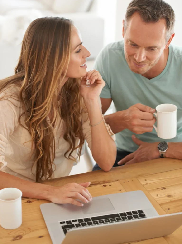 Pareja conversando frente al ordenador con una taza de café, simbolizando el intercambio de experiencias sobre aprendizaje online